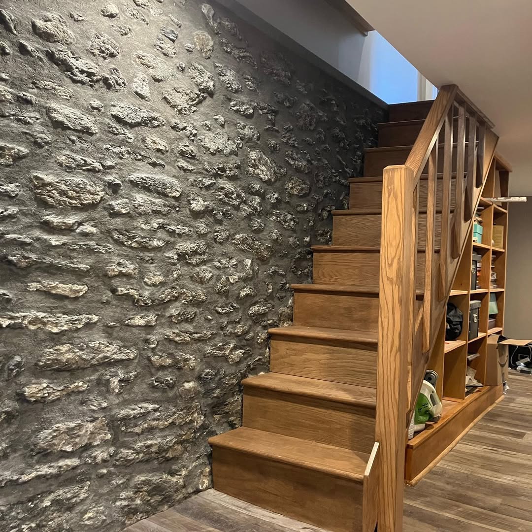 Wood staircase and built in shelving beside an exposed stone wall in a Sehnco renovation